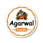 The image features the official logo of Agarwal Foods on a clean white circular background. The logo includes an artistic illustration of traditional Indian spices and herbs at the center, featuring garlic, red chili, green leaves, and dried spices, symbolizing authentic flavor and natural ingredients. Surrounding the logo is an elegant orange decorative circular border. The brand name “Agarwal” appears prominently in bold black text, while “Foods” is displayed below inside an orange rounded rectangle with white lettering. The overall design reflects freshness, authenticity, and the traditional essence of Indian spices and food products.